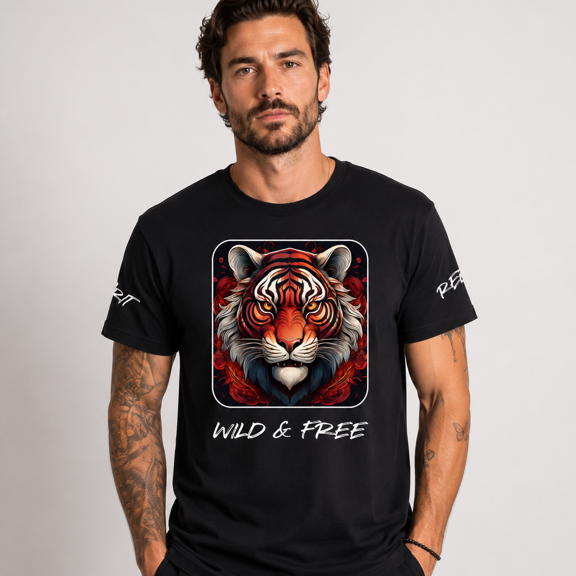 A man wearing a black crew-neck t-shirt with a large graphic of a tiger's face in red, orange, and white, with the text 'WILD & FREE' printed below it. The background is a solid light gray studio backdrop.