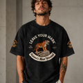 A man wearing a faded black graphic t-shirt with a tiger and 'Leave Your Mark' design, paired with off-white pants, standing against a concrete wall.