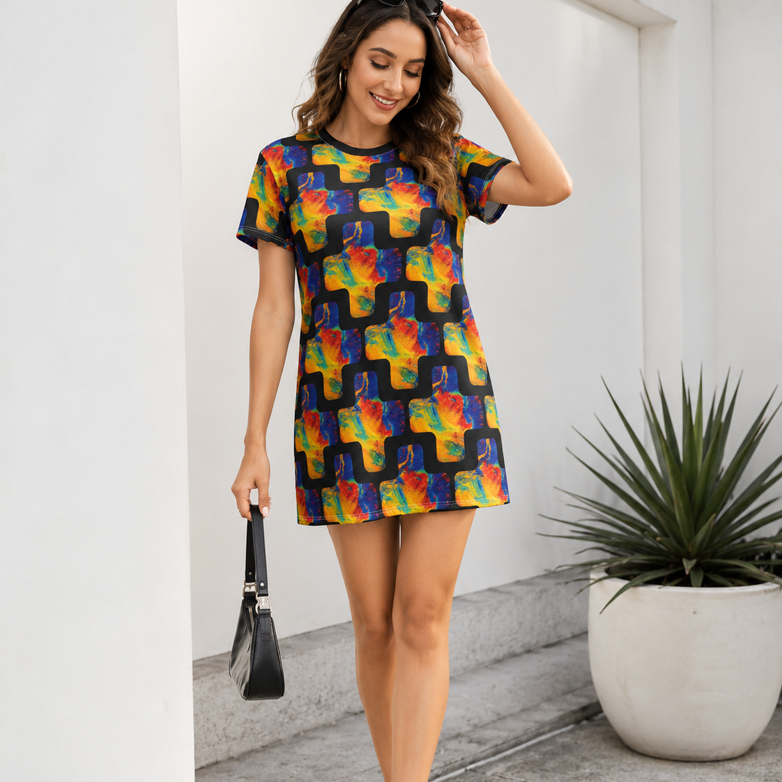 A woman models a short-sleeve mini dress with a colorful abstract print on a dark background, styled with white sneakers and a black handbag in an outdoor setting.