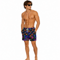 A shirtless male model wearing colorful swim trunks with a vibrant multicolor abstract pattern on a solid white background.