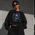A model wears a black cropped sweatshirt with a large colorful skull graphic on the front, shown in a three-panel collage against a concrete wall. The panels show the front view, back view, and seated view.